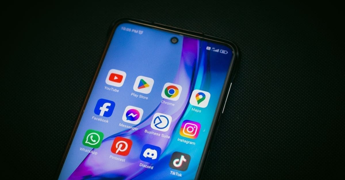 Close-up of a smartphone screen showing colorful app icons (YouTube, Play Store, Chrome, Maps, Facebook, Instagram, WhatsApp, Pinterest, Discord, TikTok) on a dark background.