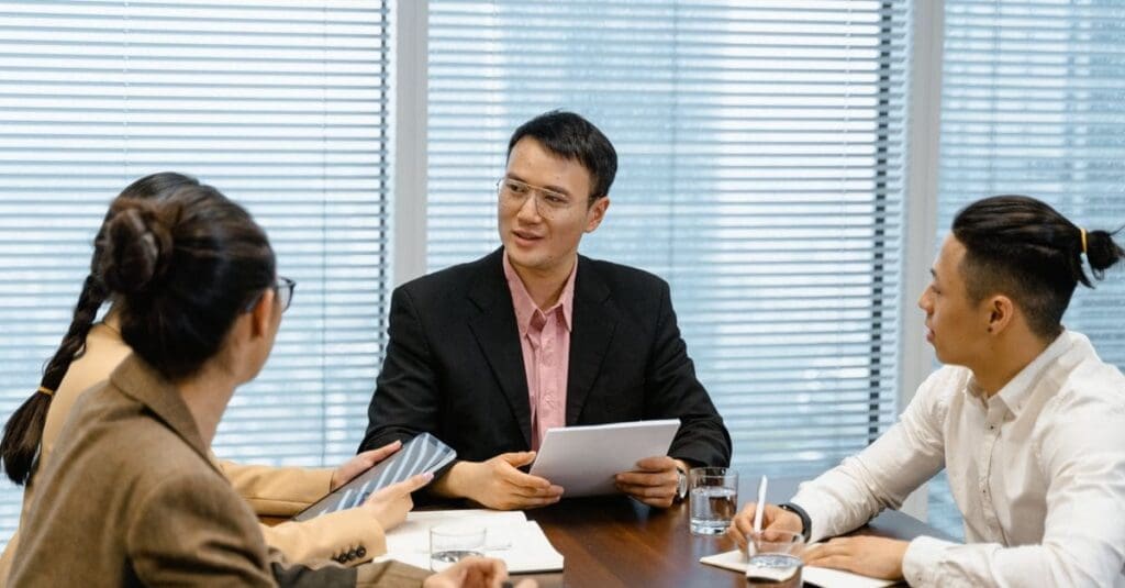 downloaded-image Group of four professionals in a meeting around a wooden table, discussing documents and notes.