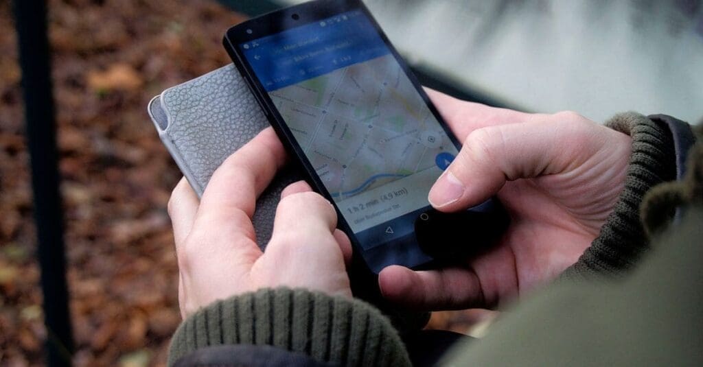 downloaded-image Person holding a smartphone showing a map navigation app outdoors, with a route visible on screen.
